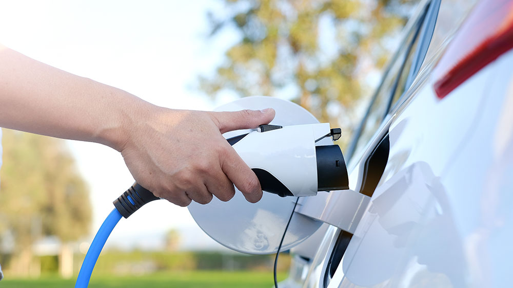 Electric car or ev is charging at station . man use the white power cable and plug on nature background.