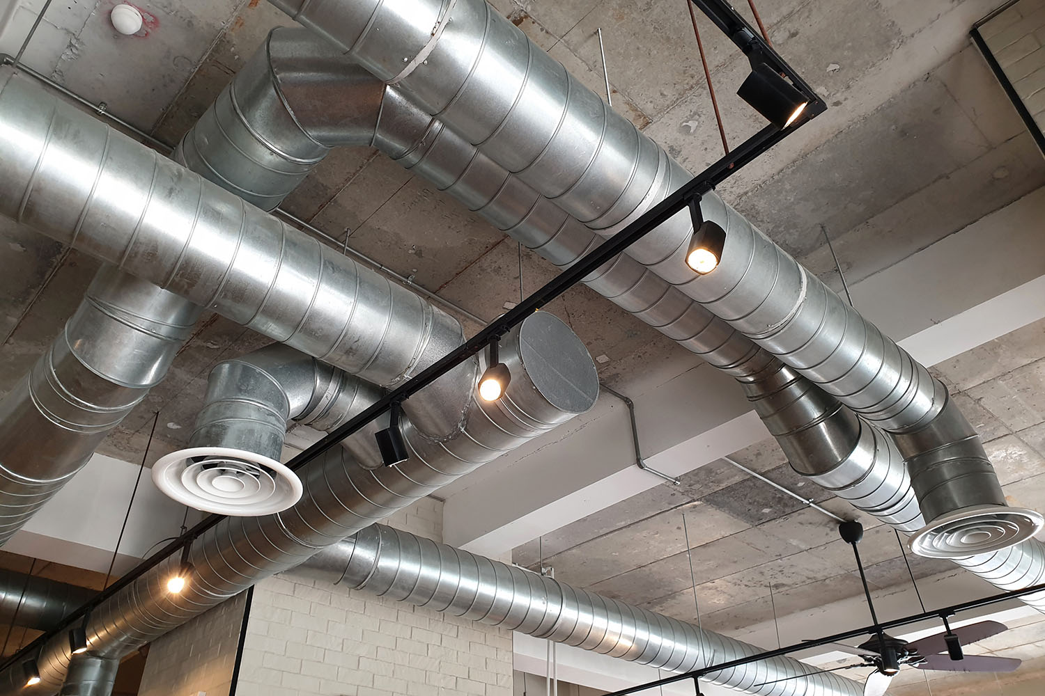 Ventilation pipes in silver insulation material hanging from the ceiling inside new building.